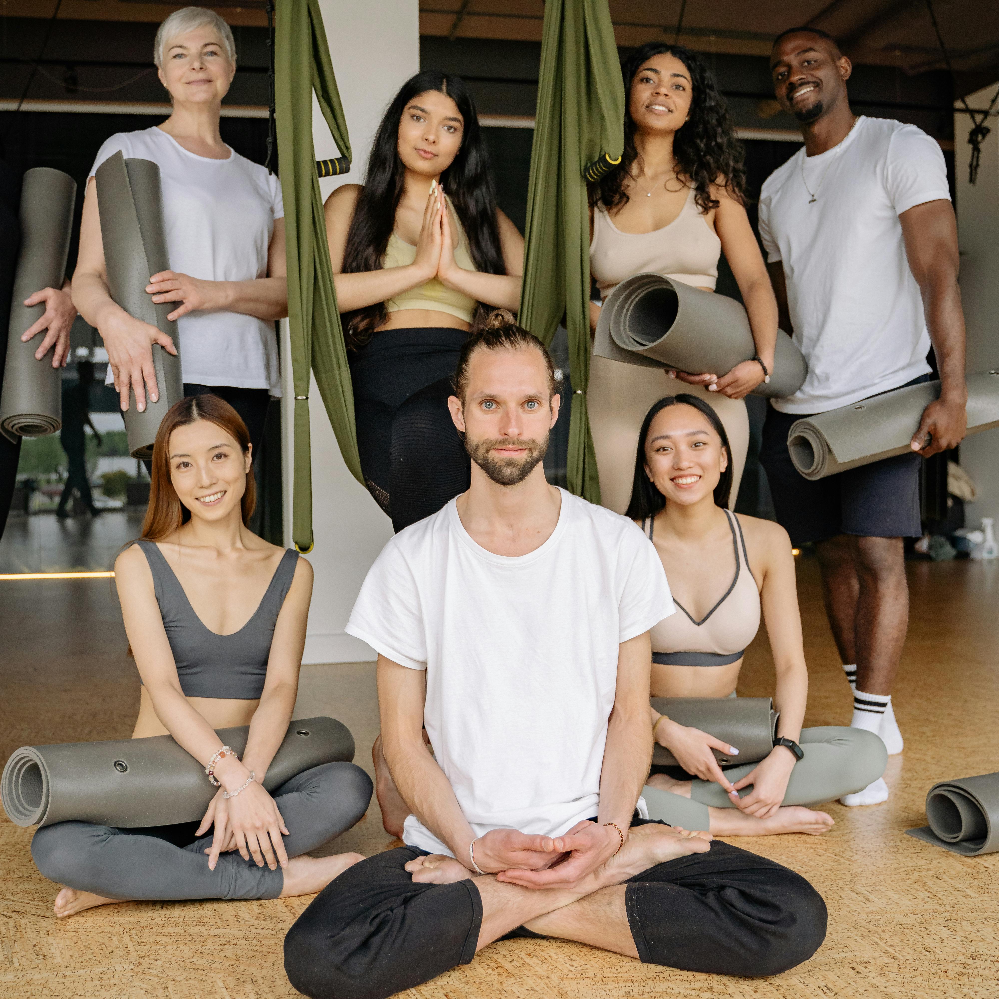 A diverse group of people in activewear enjoying a yoga class together with mats and smiles in a studio setting.