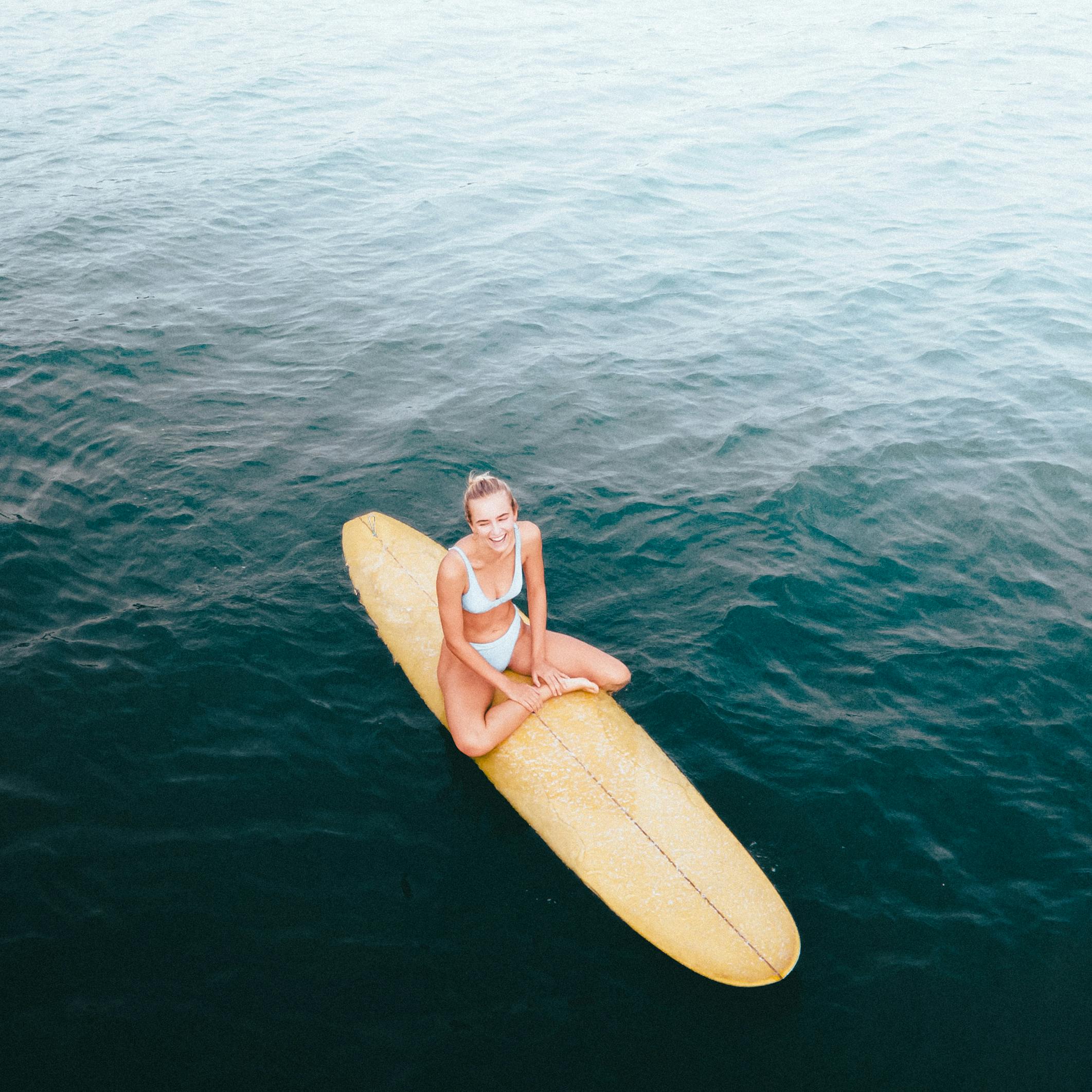 Woman in bikini on surfboard in the ocean, captured from above. Perfect for summer and adventure themes.